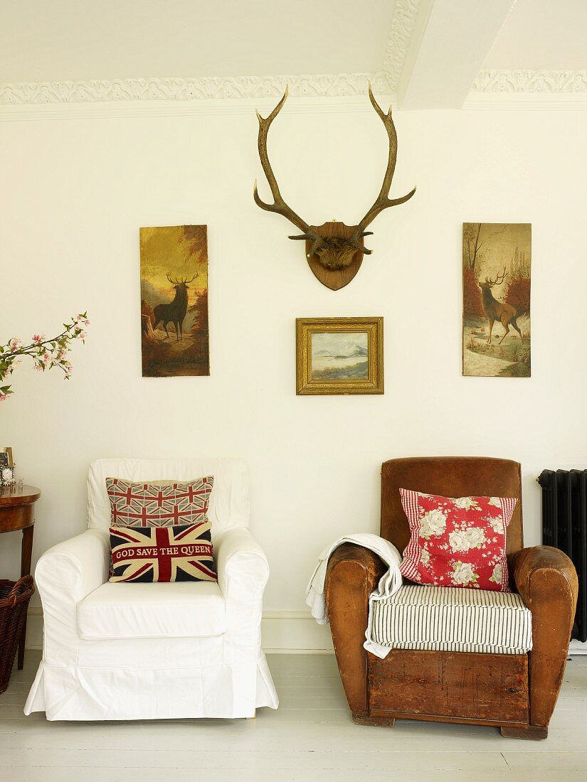 Polsterstühle mit Dekokissen, Wandbilder mit Jagdmotiven und Hirschgeweih im Wohnzimmer