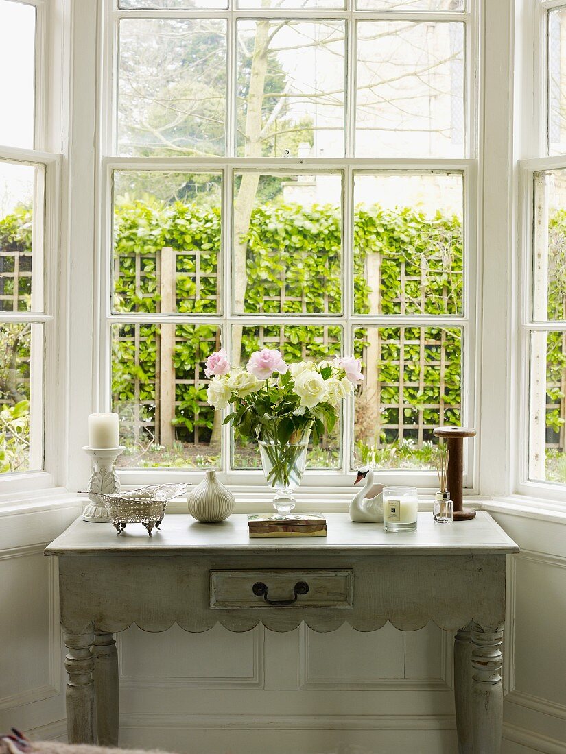 Beistelltisch mit Blumenstrauss und Dekogegenständen vor einem Fenster mit Gartenblick