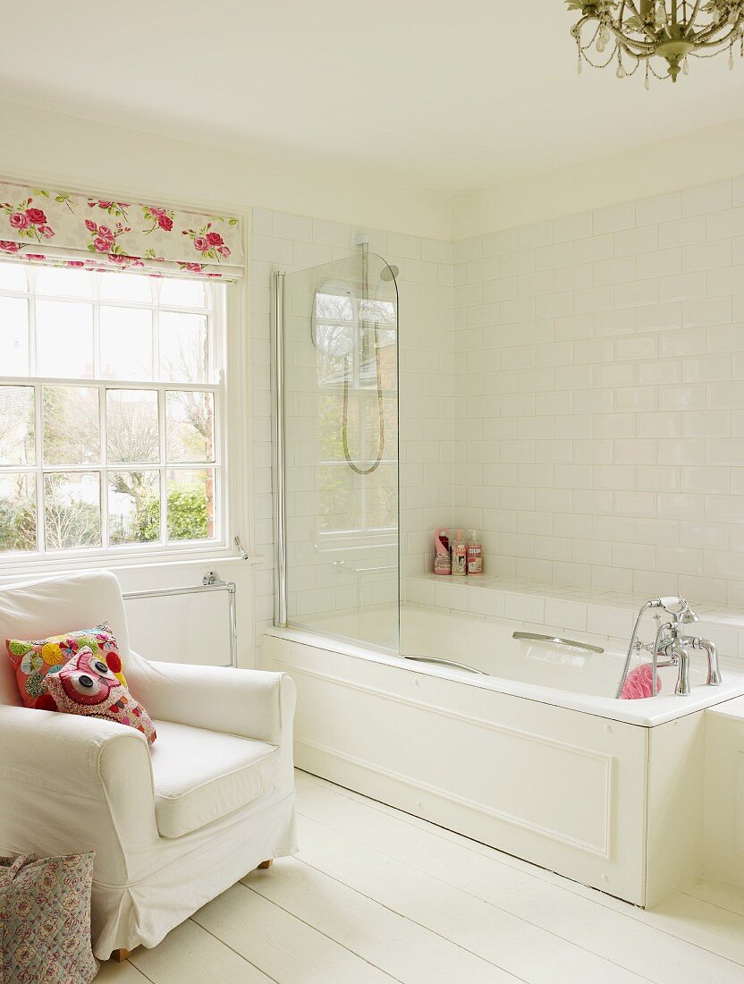Bright bathroom with bathtub, white upholstered armchair and white wooden floor