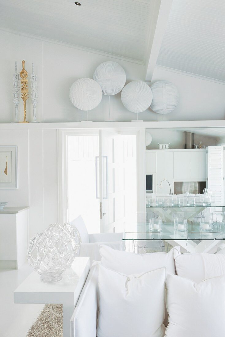 Blick über weiße Kissen und Sitzbank auf weiss lackierte Schild-Sammlung und Ablage über der Tür in weißem Designer Wohnraum