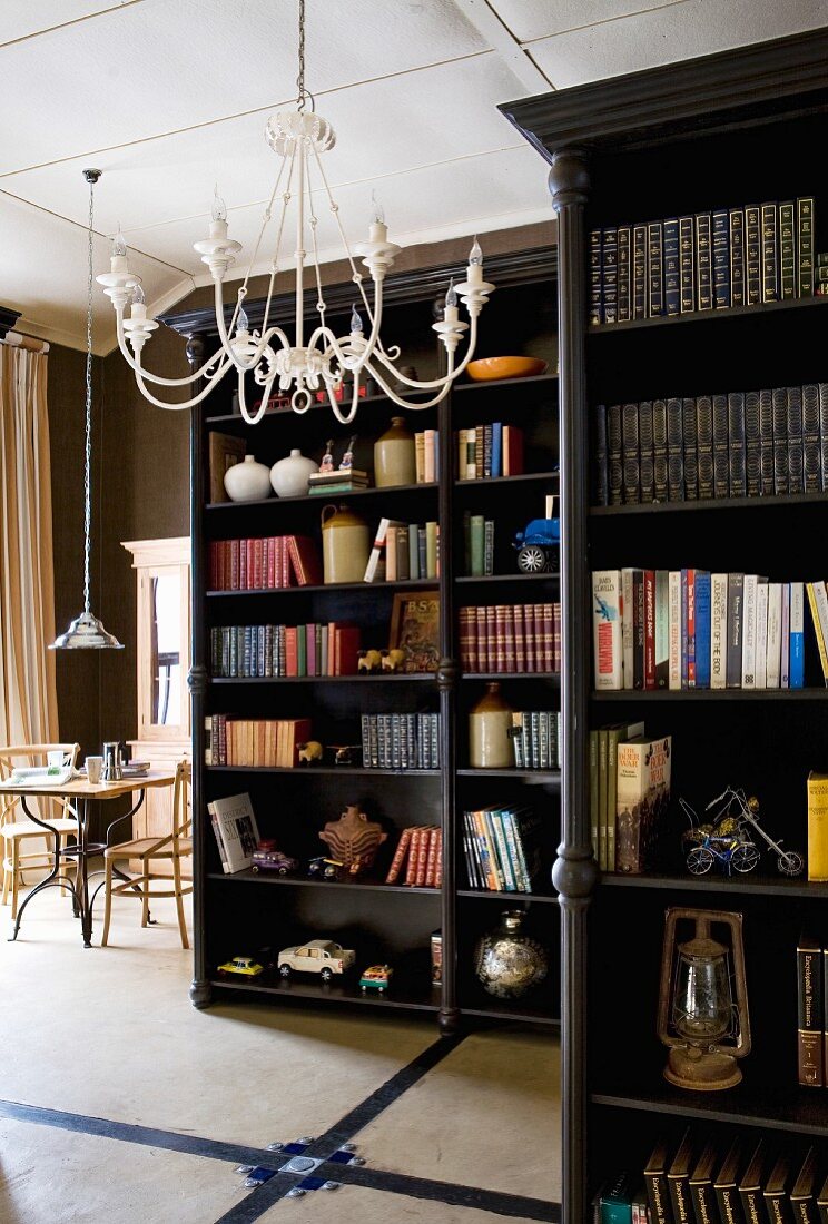 Dunkel lackierte Bücherregale im Raum stehend und weisser Metall Lüster an Decke in offenem Wohnbereich