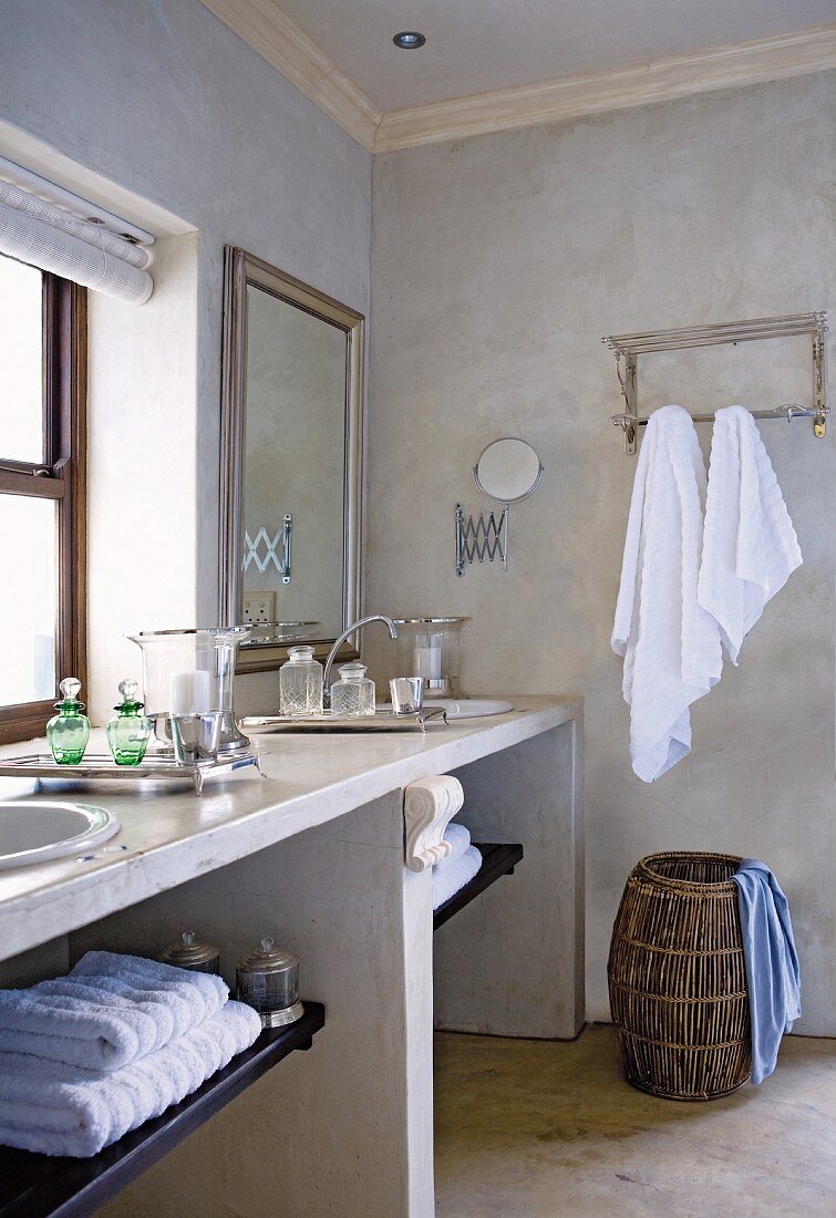 Waschtisch aus Stein mit zwei Waschbecken, Wäschekorb und aufgehängte Handtücher im Badezimmer