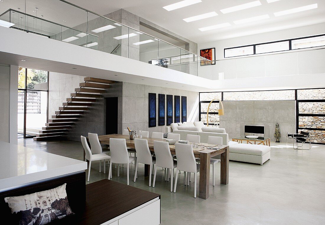 Offener, grosszügiger Designer Wohnraum mit Essplatz auf Estrichboden und Blick auf umlaufende Galerie mit Treppenaufgang in zeitgenössischer Architektur