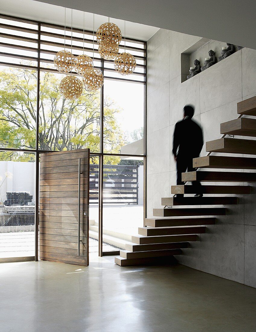 Minimalistische Treppe mit auskragenden Holzstufen in Foyer mit Glasfassade und offener Haustür