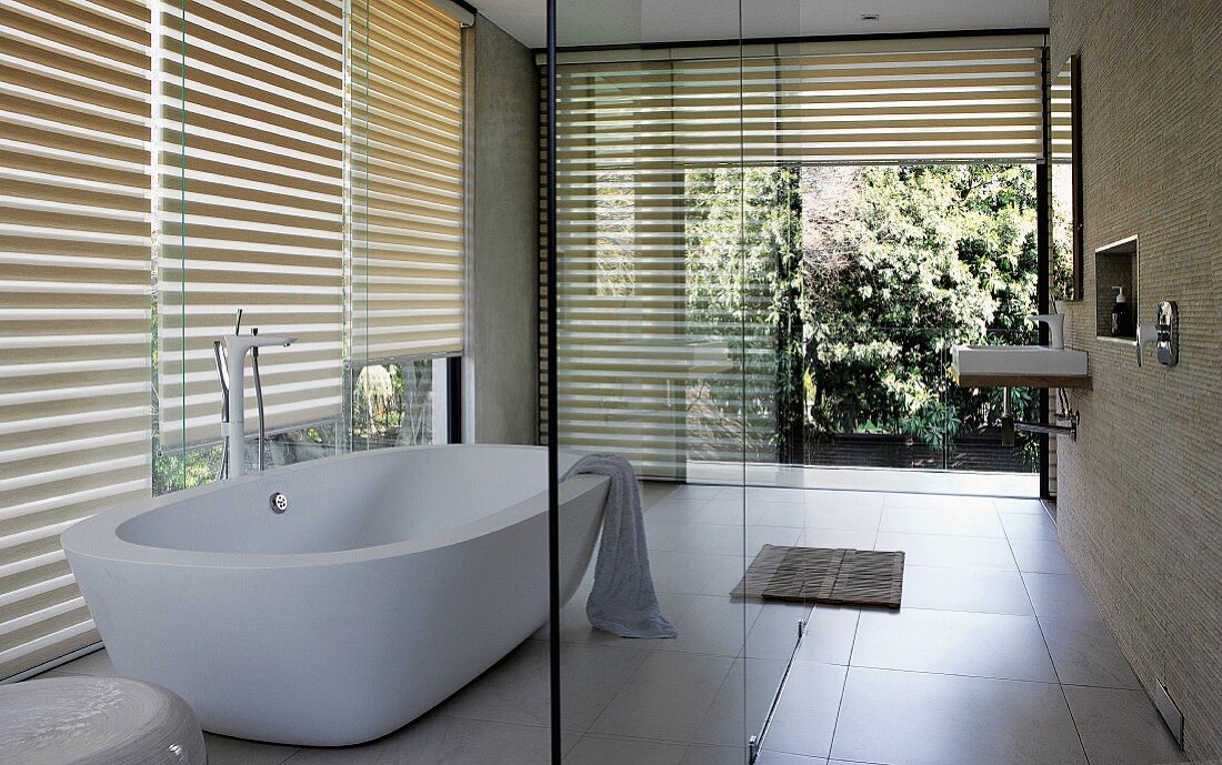 Designer bathroom with free-standing bathtub in front of glass wall with half-closed louver blinds
