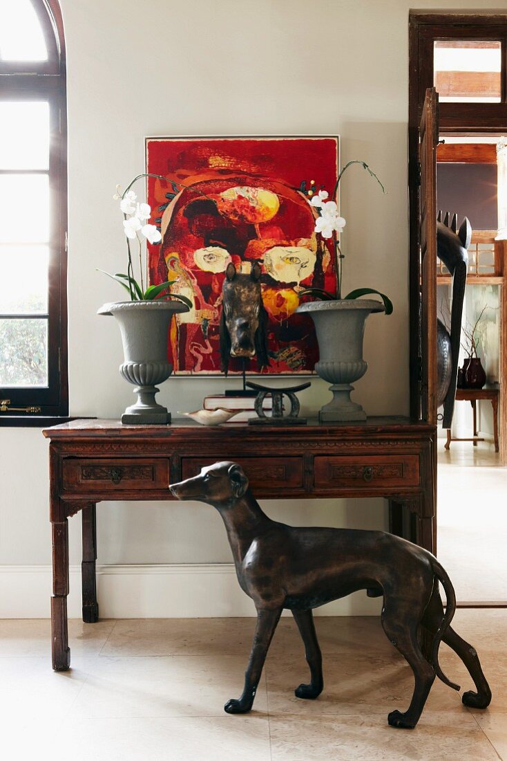 Antique console table below modern painting on white wall; life-size bronze of greyhound in foreground