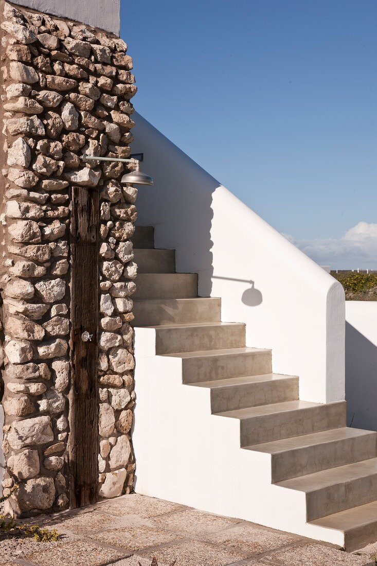 Concrete steps with white balustrade next to outdoor shower on rustic stone wall