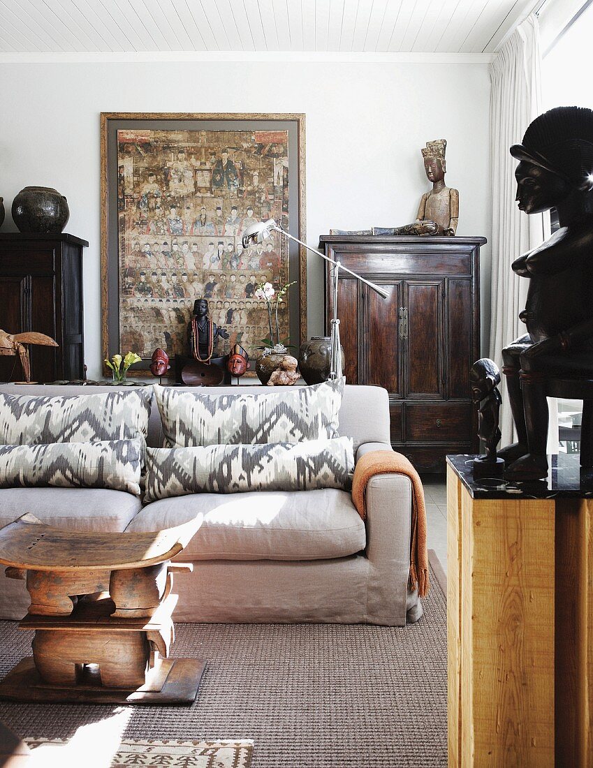 Living room with antique, Chinese wooden furniture and objets d'art from around the world; sofa with soft upholstery in foreground with wooden, sculptural coffee table