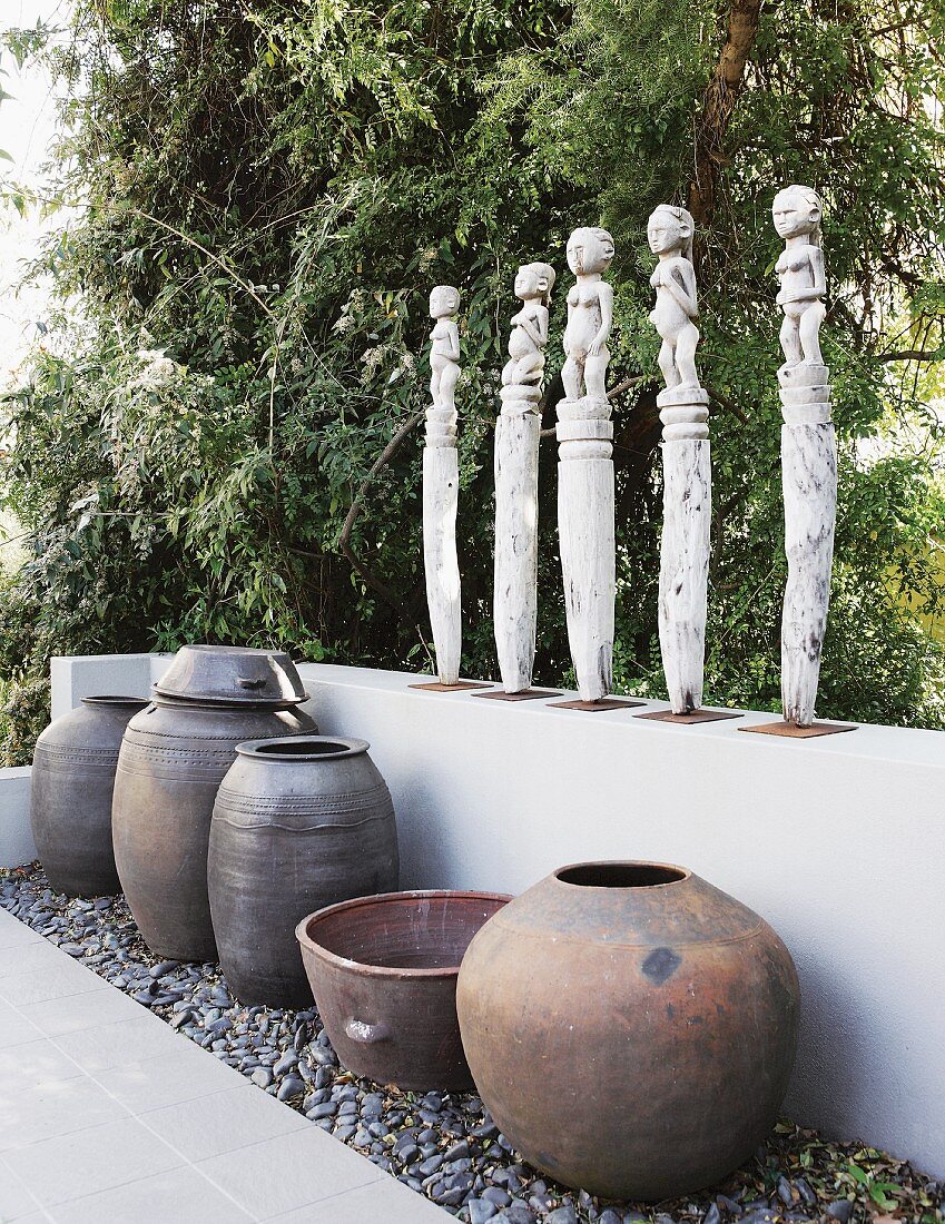 Row of statues of women on low wall above collection of large vases