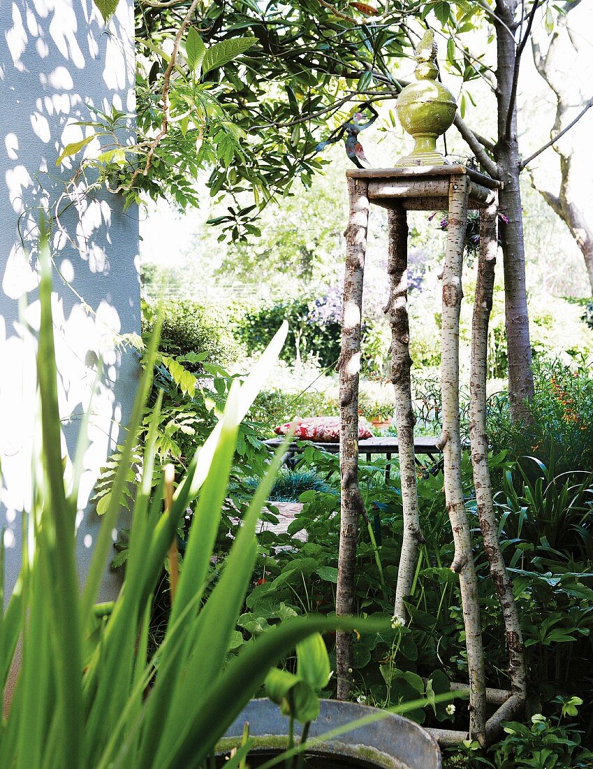Garden sculpture on pedestal made from branches next to corner of house in sunny garden