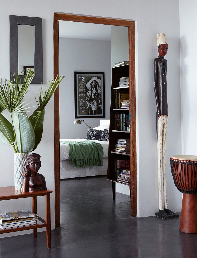 Objets d'art and djembe in front of doorway leading to bedroom; wooden door frame contrasting with polished concrete floor