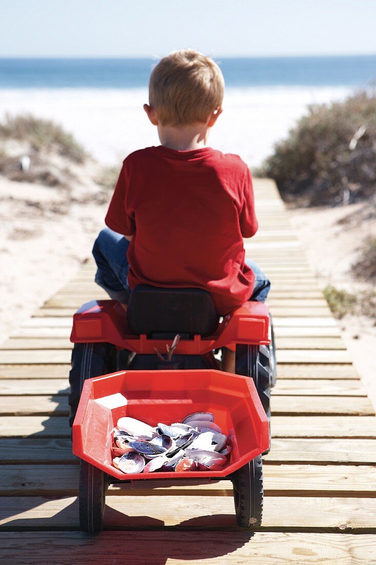 Little boy on toy tractor driving along a wooden boardwalk