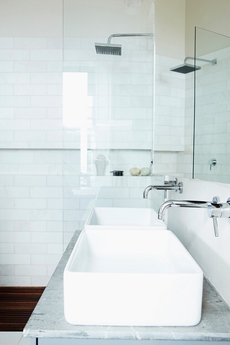 Duschraum mit quadratischem Brausenkopf und weissen Wandfliesen; vor der Glastrennwand ein Marmorwaschtisch mit zwei rechteckigen Waschschüsseln