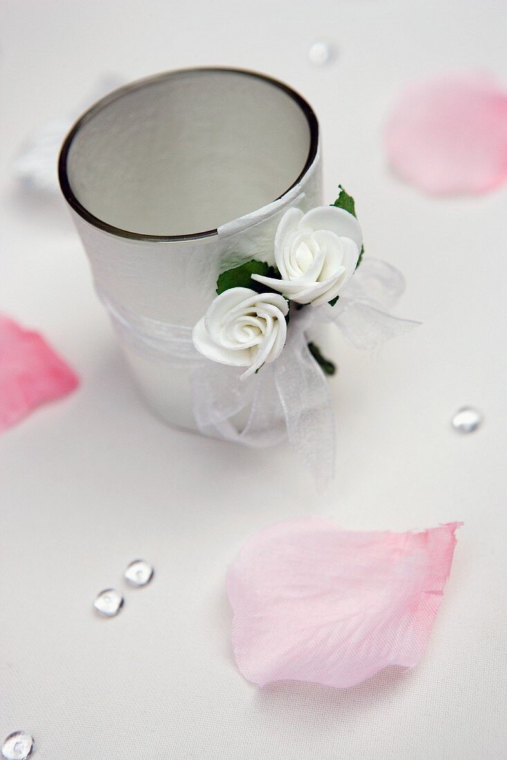 Tealight holder decorated with ribbon and white flowers amongst scattered rose petals
