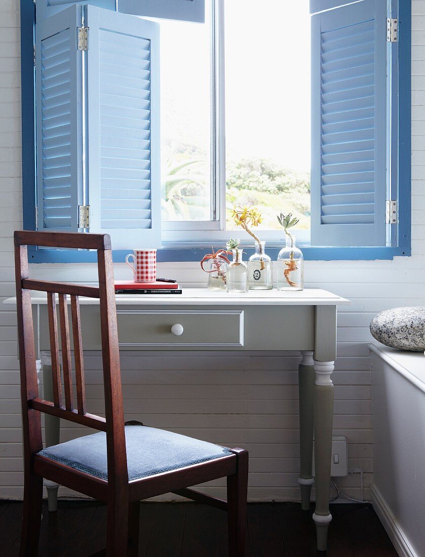 Pastellblaue Fensterläden und darunter stehender, weisser Vintage Tisch mit Sukkulenten in Glasväschen