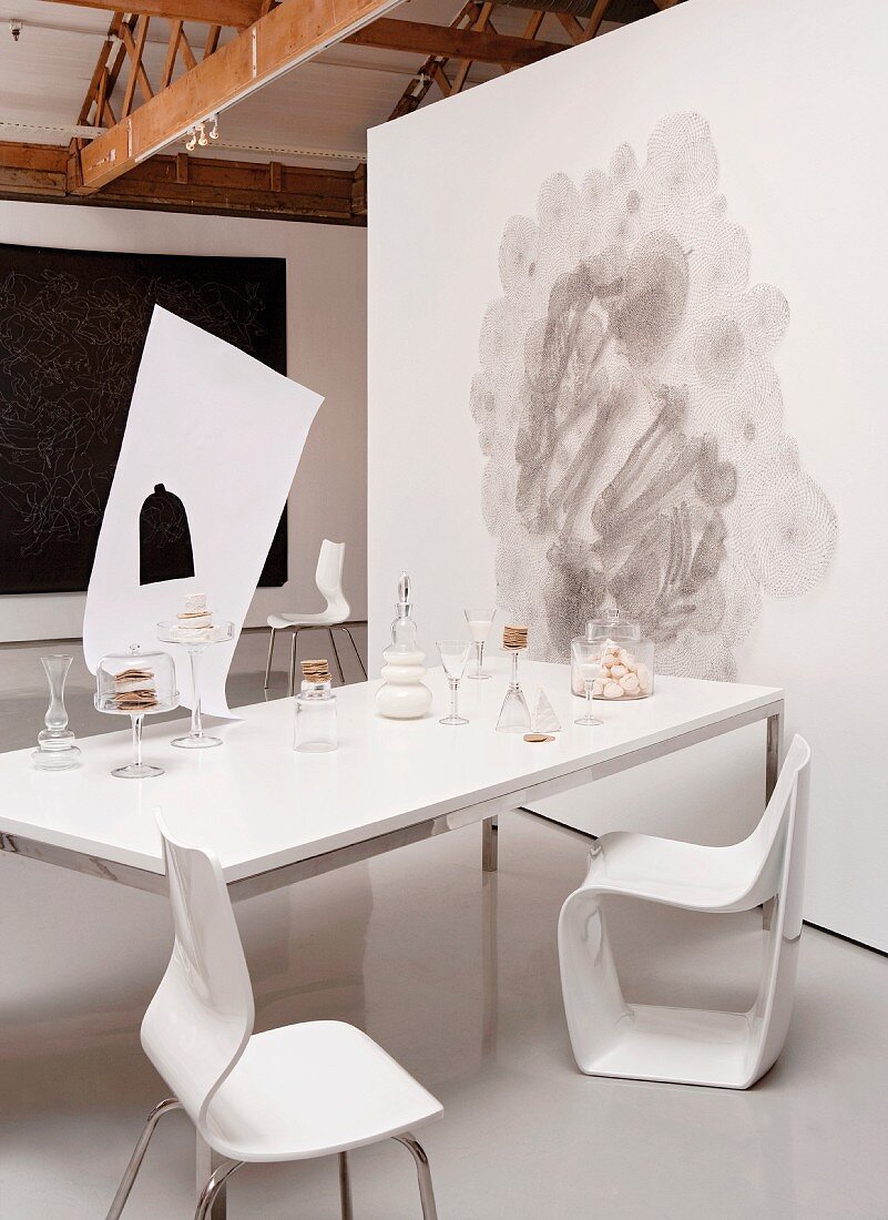 Gedeckter Tisch mit Keksen in einem Raum mit grauem Kunstoffboden, Wandgrafik, Wandteppich und offenem Dachstuhl