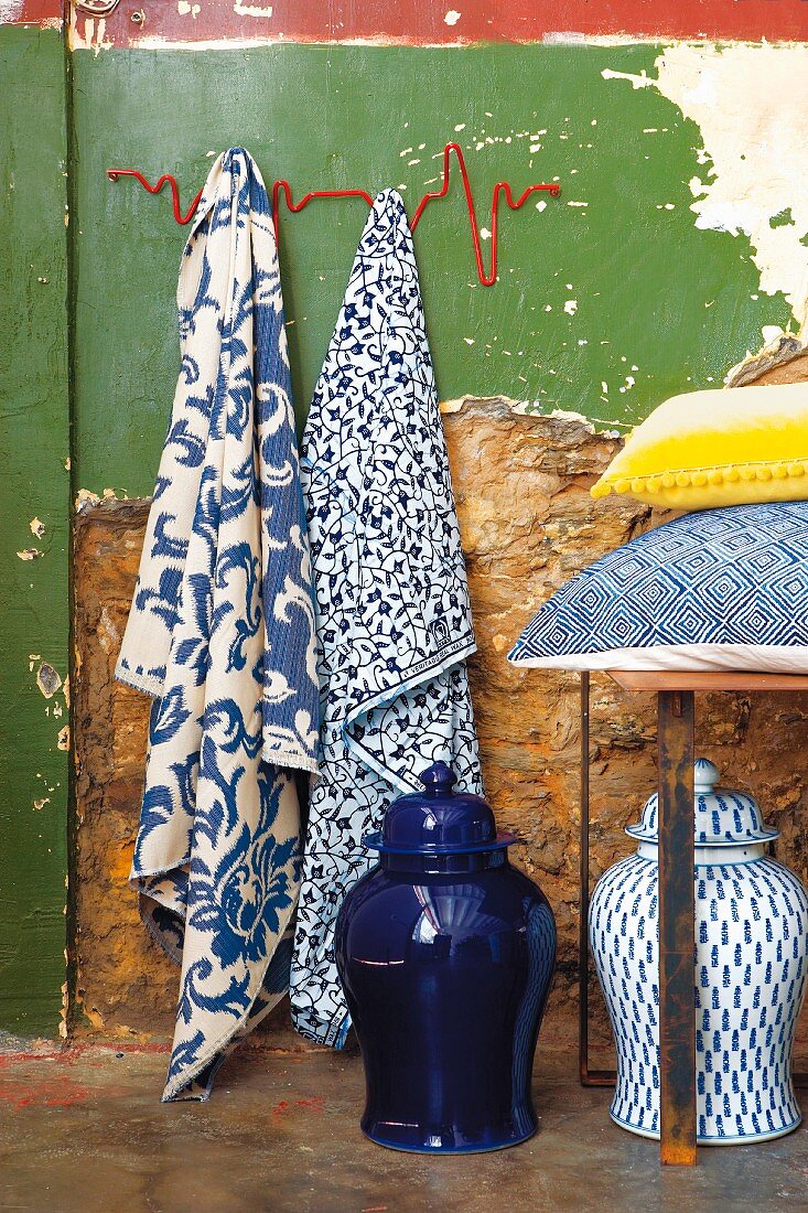 Blue and white patterned tea towels on wall hooks, storage jars and scatter cushions on bench