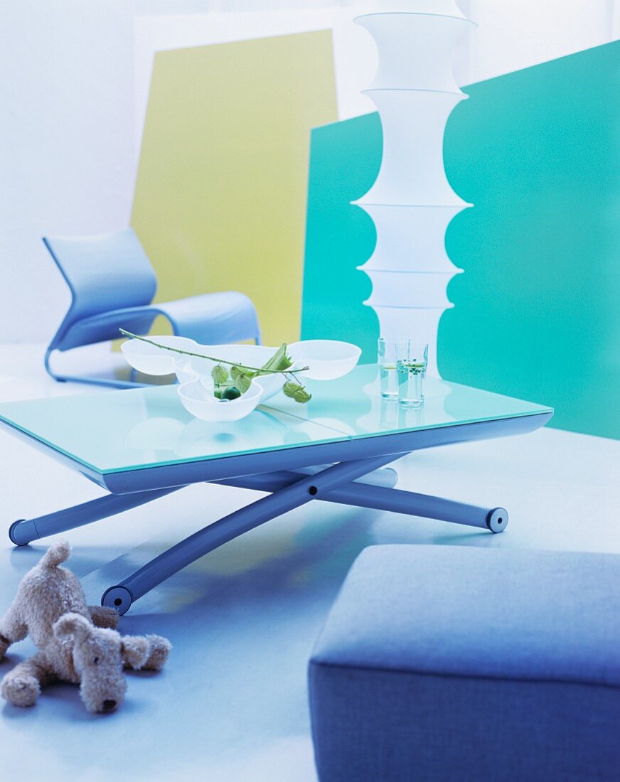 Moderner Couchtisch mit Metallgestell und Sessel vor zylinderförmiger Deckenlampe und farbigen Paneelen