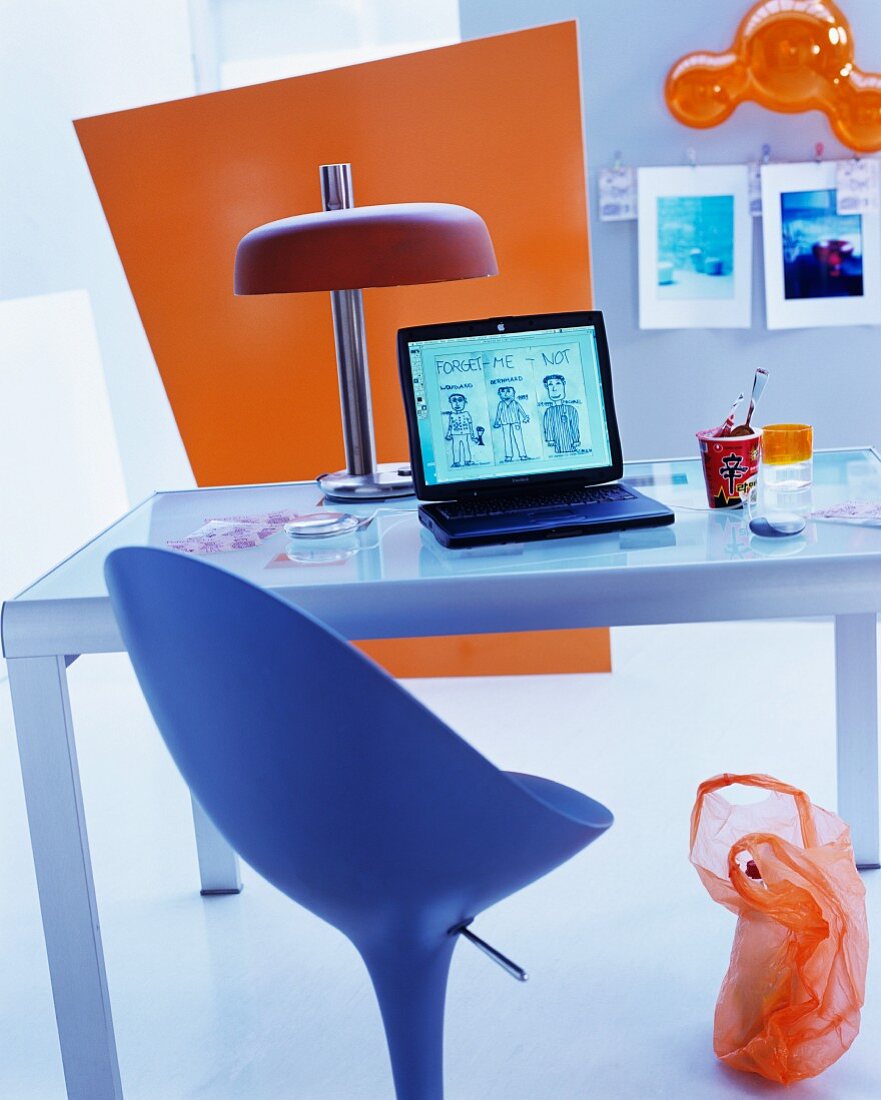 Designer swivel chair in front of retro table lamp on glass desk and coloured panel