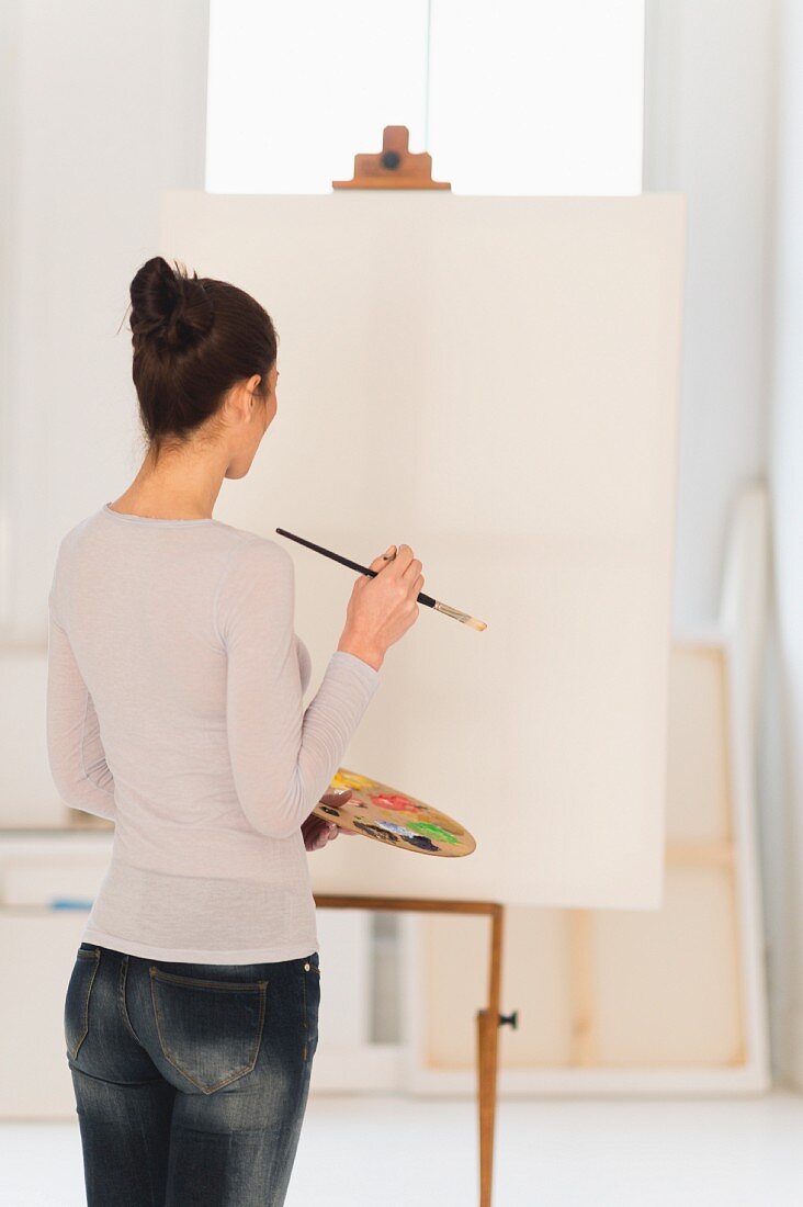 Frau vor einer leeren Leinwand auf einer Staffelei im Künstleratelier