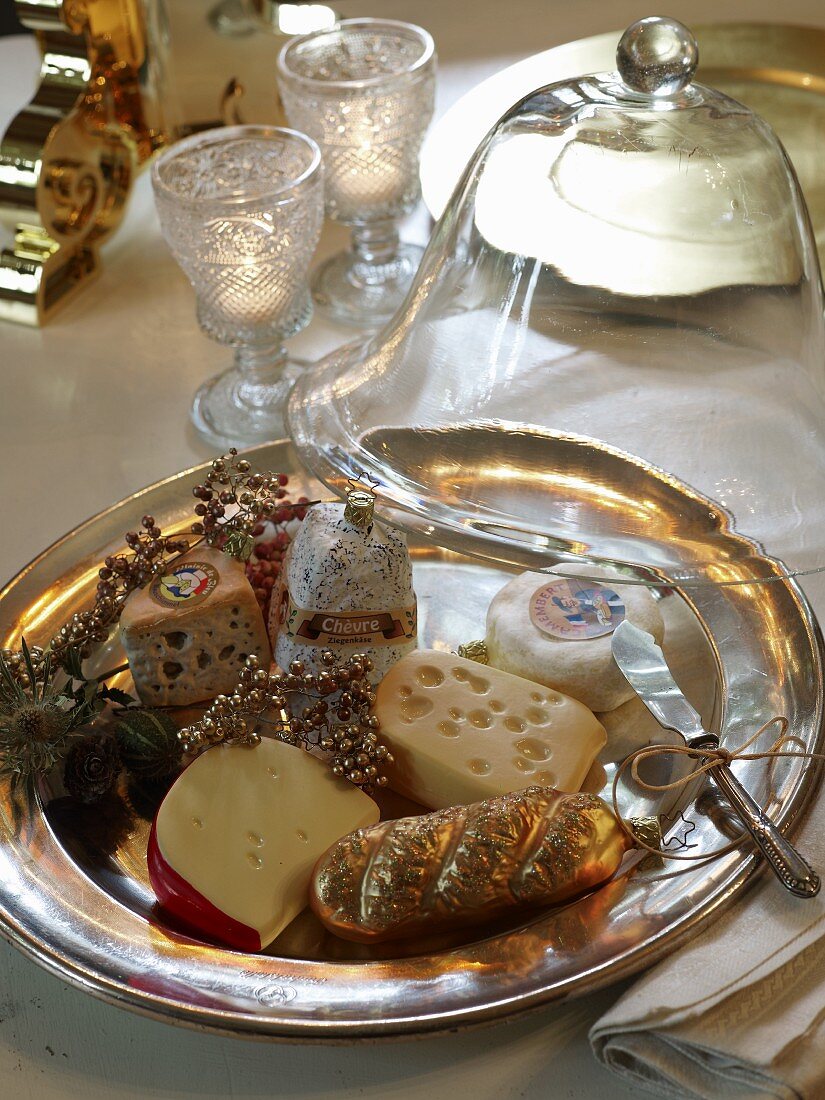 Platter of various cheese-shaped ornaments under half-open glass cheese cover