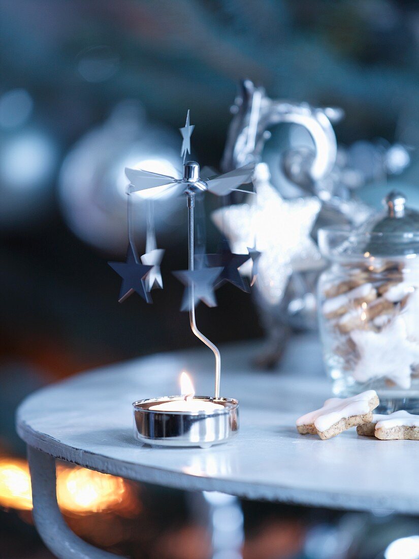 Teelicht-Karussell mit brennender Kerze neben Weihnachtsplätzchen im Aufbewahrungsglas auf Beistelltisch