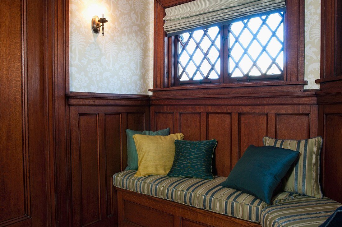Cushions on wooden bench built into wooden wall panelling below window