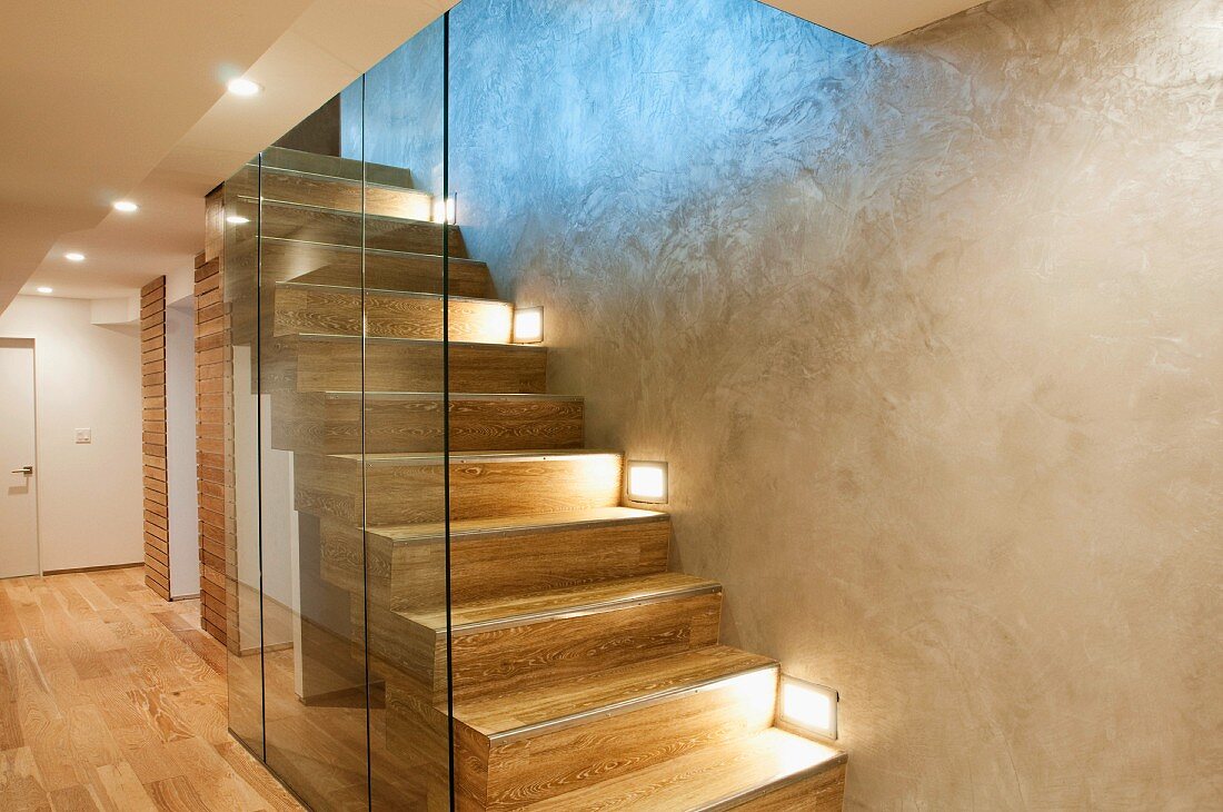 Glastrennscheibe vor moderner Treppe mit Einbauleuchten in Wand eines minimalistischen Treppenhauses