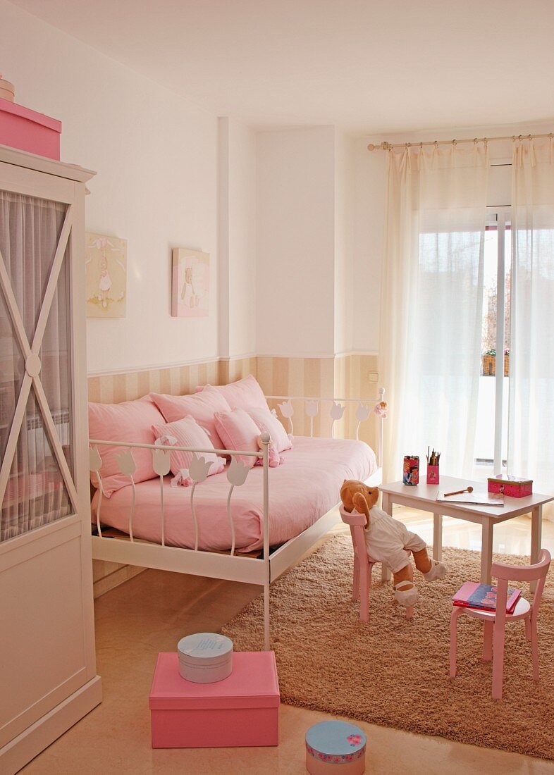 Charming girl's bedroom in pale pink with metal bed as sofa and teddy bear on child's table