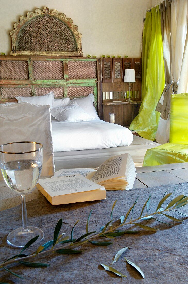 Tisch mit Olivenzweig und Glas vor Doppelbett mit weisser Bettwäsche in schlichtem Schlafzimmer