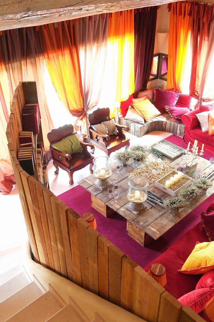 Blick von Treppe in Loungebereich mit Raumteiler aus Holz und grosser selbstgebauter Tisch mit Kerzenständern vor Fenstern mit geschlossenen, lichtdurchflutenden Vorhängen