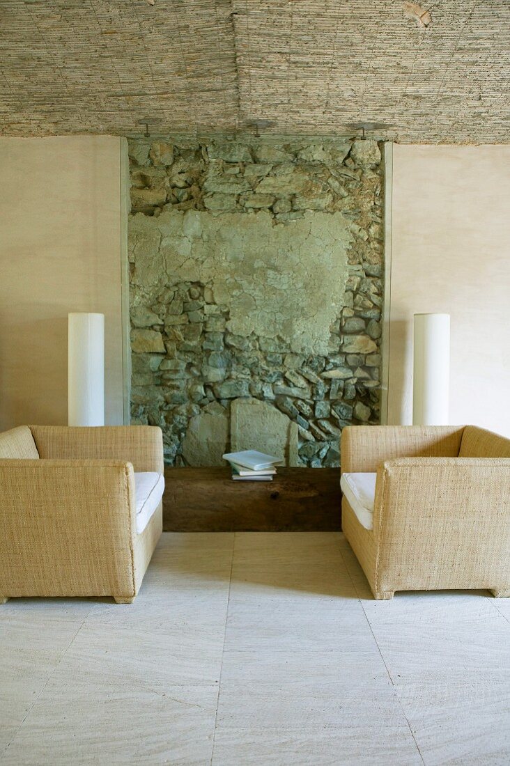 Sesselpaar vor einem Stück unverputzter, alter Bruchsteinwand als besonderer Akzent in renovierter, mallorquinischer Finca