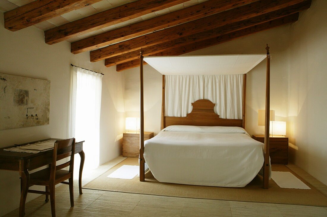 Natural materials and colours in Majorcan bedroom with canopied bed and small writing desk