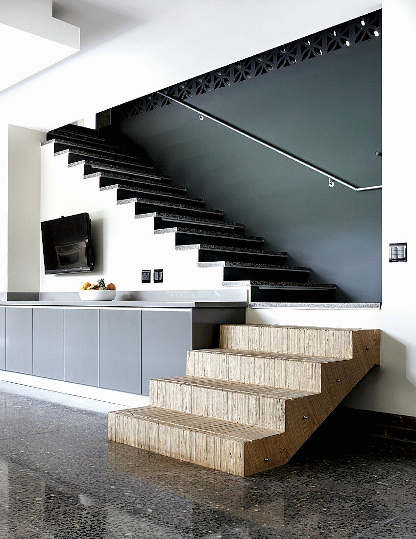 Stufenelement aus Sperrholz an Stirnseite eines Sideboards, kombiniert mit Terrazzo-Boden und Steinstufen auf Wohnraumtreppe