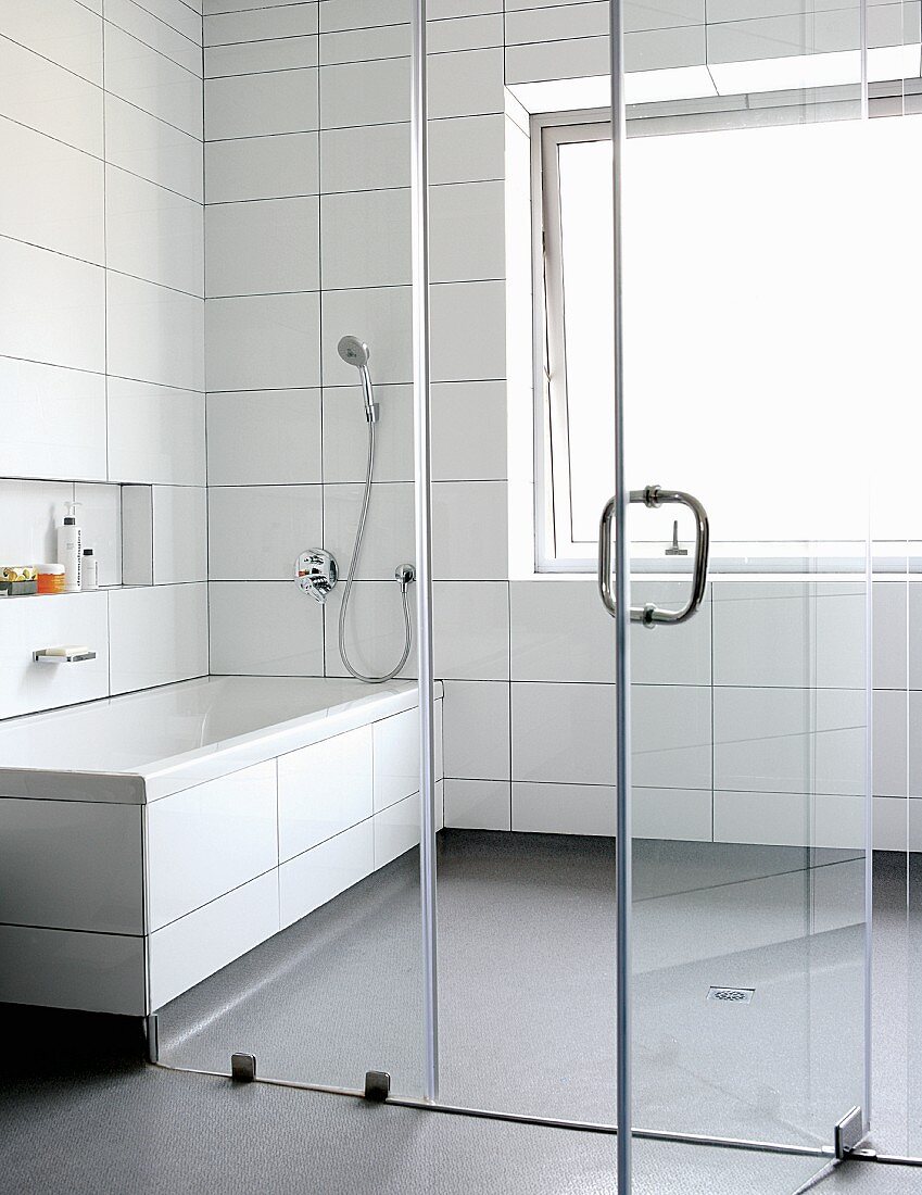 Bathroom with white tiles and grey plastic flooring separated by glass wall