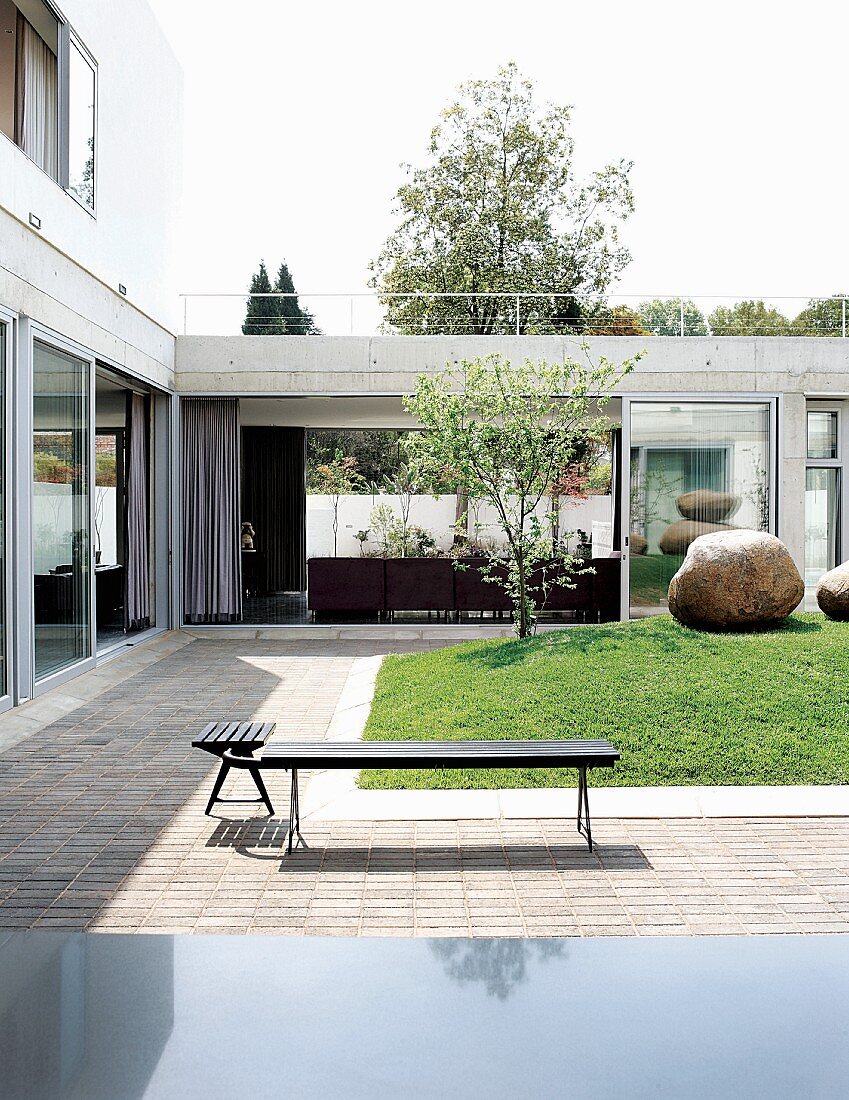 Courtyard of low house with corner bench on terrace running around central lawn with large boulders