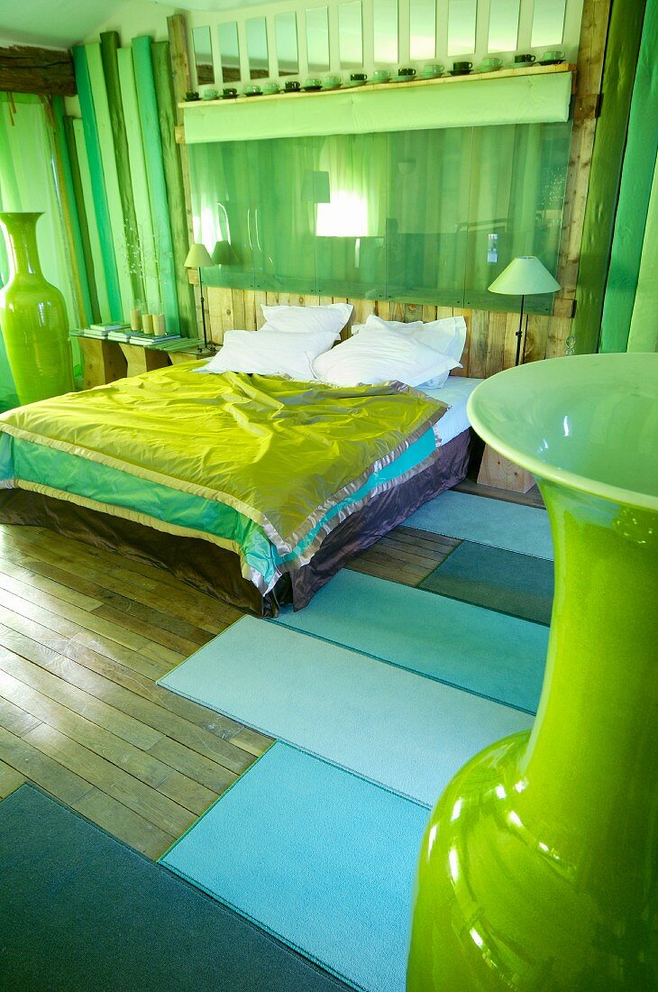 Double bed with green bedspread in rustic bedroom with tall, green floor vases