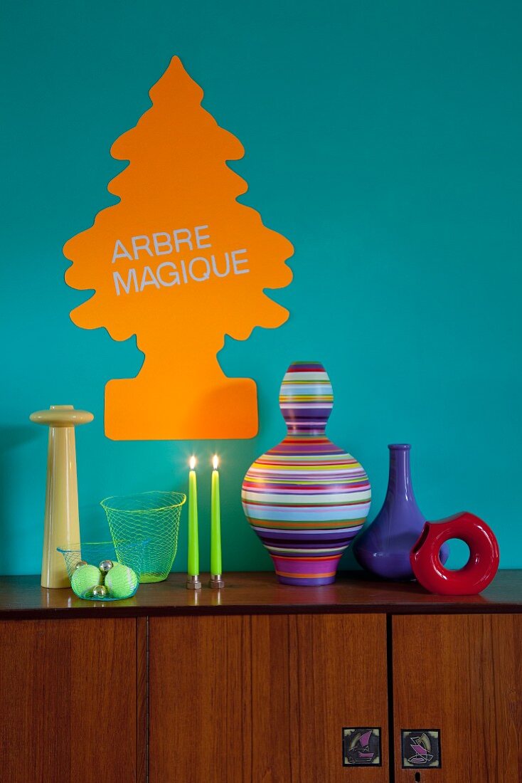 Stylised Christmas tree sticker in neon orange on turquoise wall; colourful vases and neon green candle on retro sideboard
