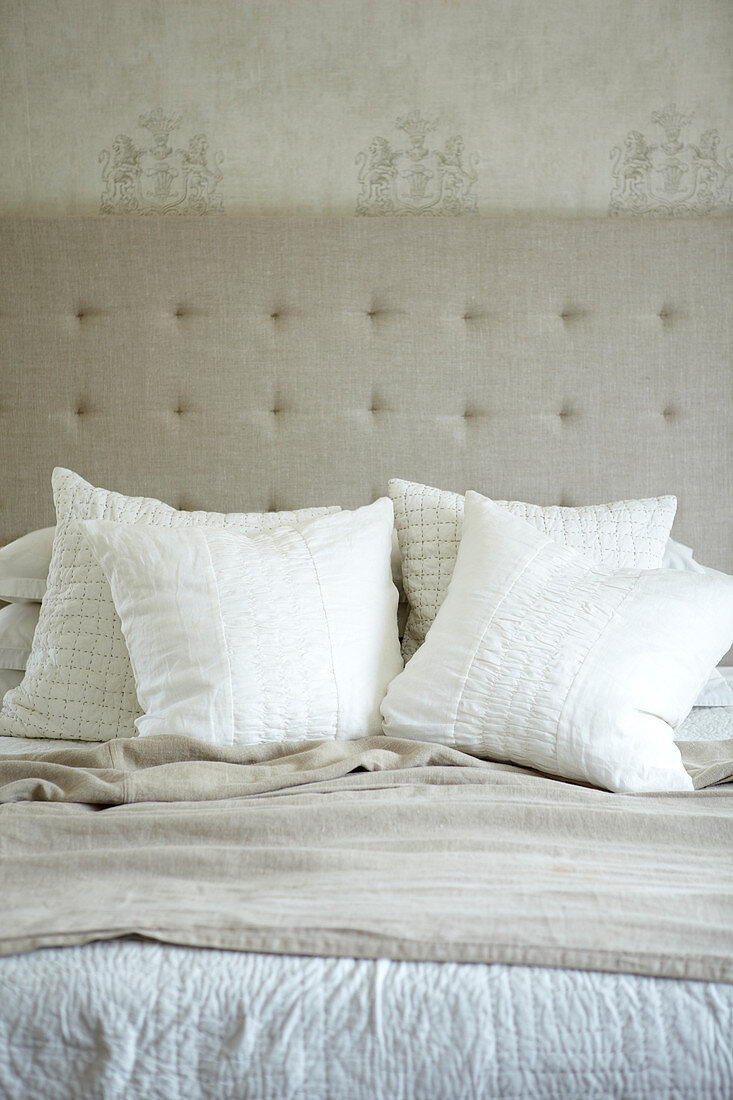Pale scatter cushions on double bed in front of headboard upholstered in linen