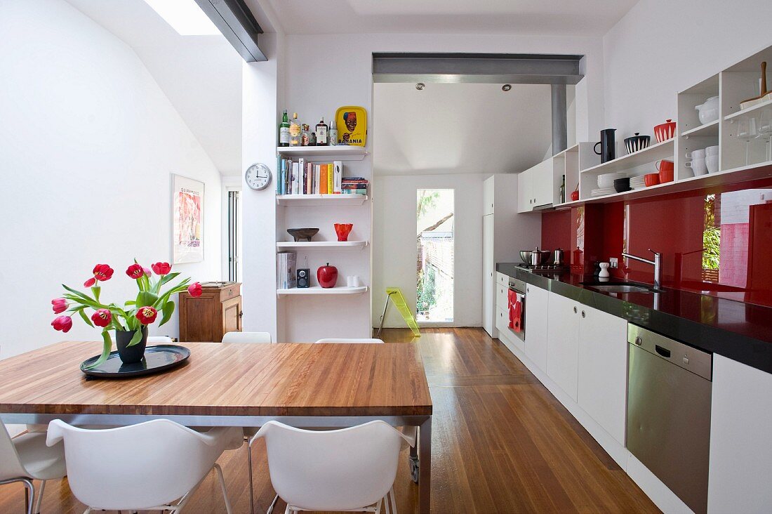 Tulpenstrauss auf Esstisch in moderner, offener Küche mit langer Küchenzeile und rotem Glas Spritzschutz