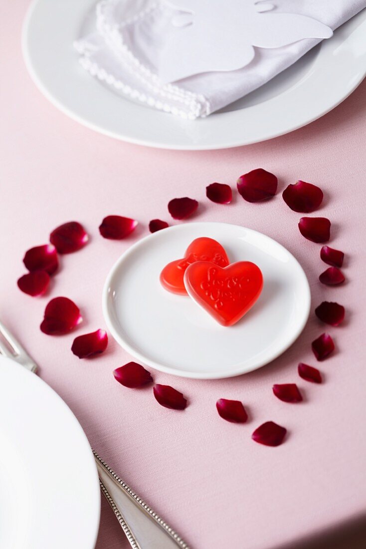Rosenblütenblätter in Herzform dekoriert um Teller mit Süßigkeiten