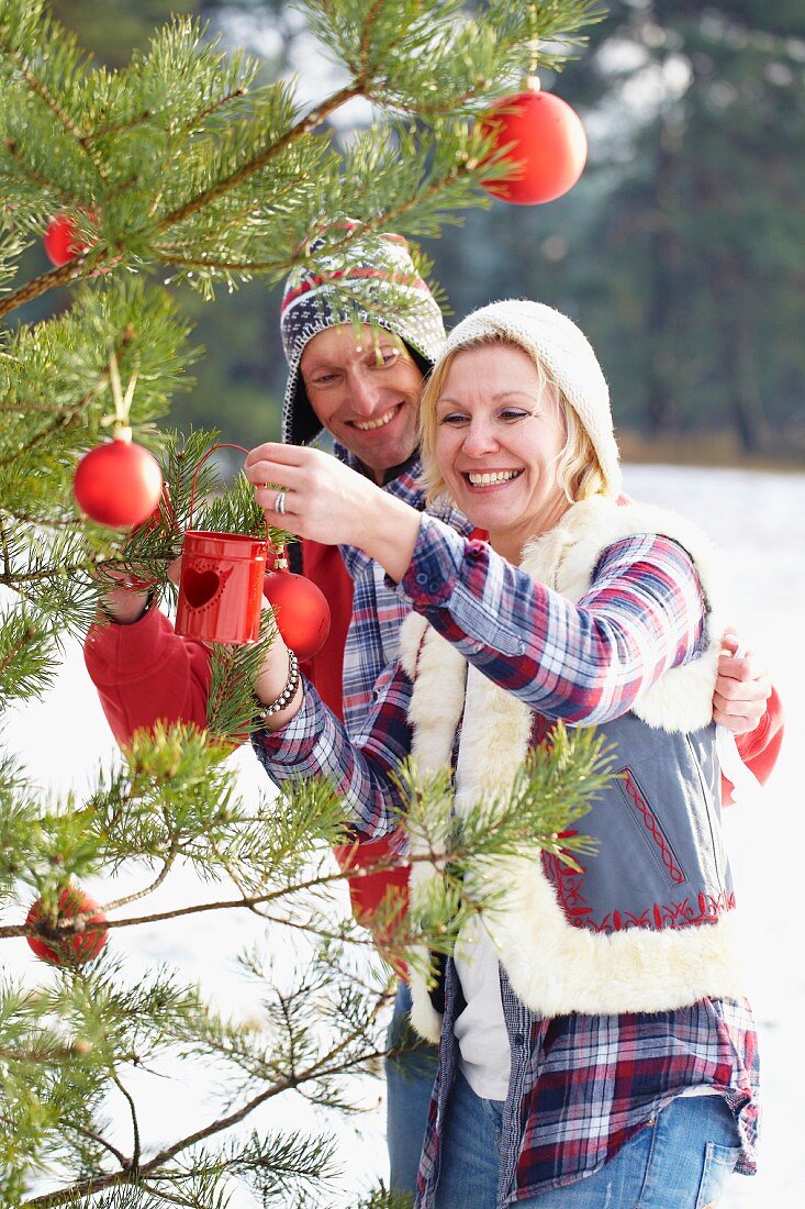 Couple decorating Christmas tree in woodland