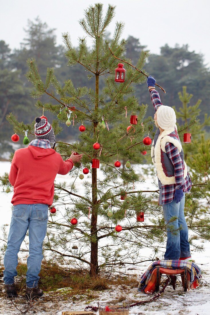 Paar schmückt einen Christbaum im Wald