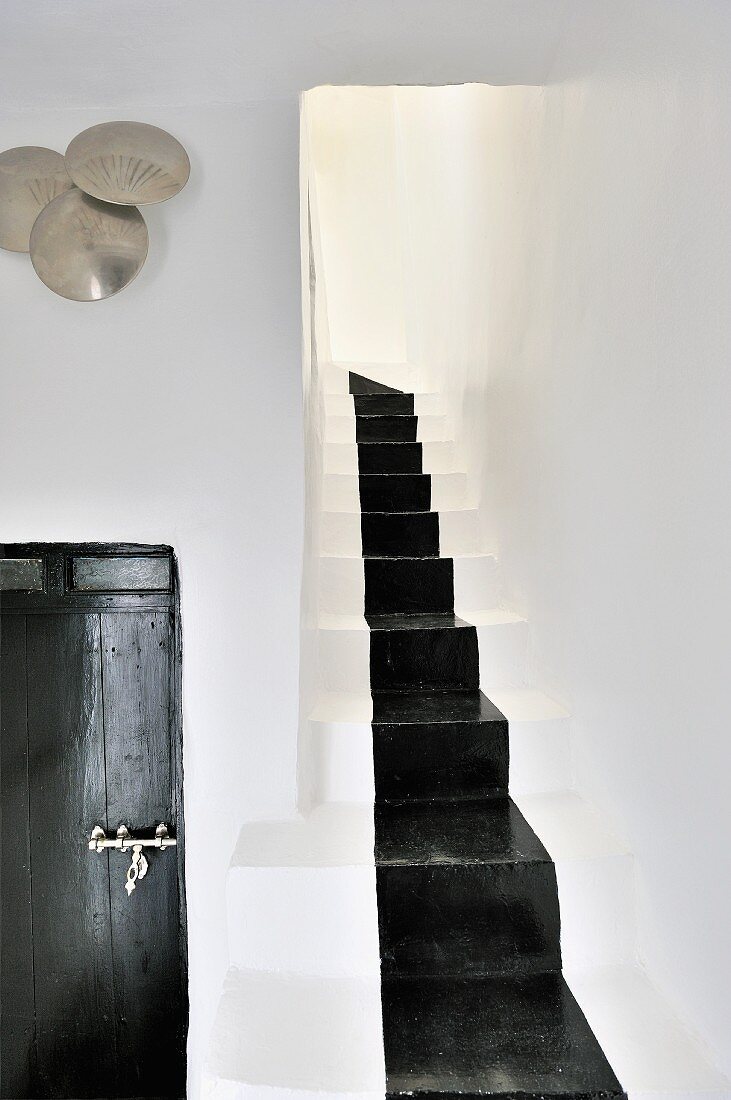 Gemauerter Treppenaufgang mit schwarz aufgemaltem Läuferband; Holztür mit marokkanischem Beschlag und gehämmerte Metallschalen an der Wand