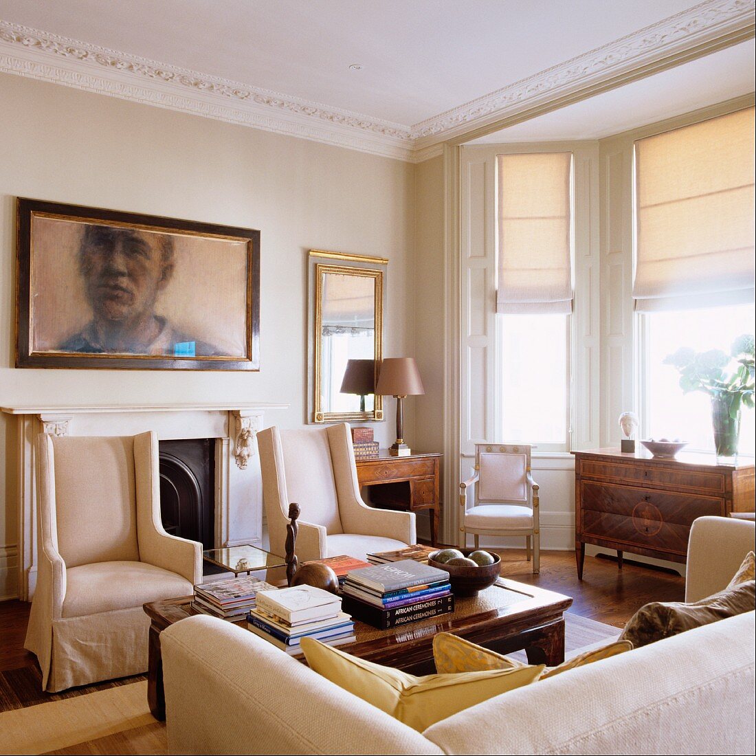 Elegante, helle Sesseln vor Wand mit Portrait im Wohnzimmer mit Stuckfries an Decke und Erker