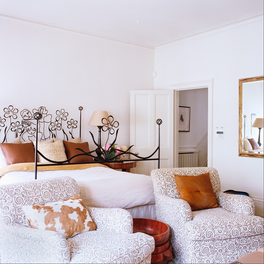 Polstersessel mit Ornamentmuster auf Bezug vor Bett mit Metallgestell und floralen Motiven in schlichtem Schlafzimmer