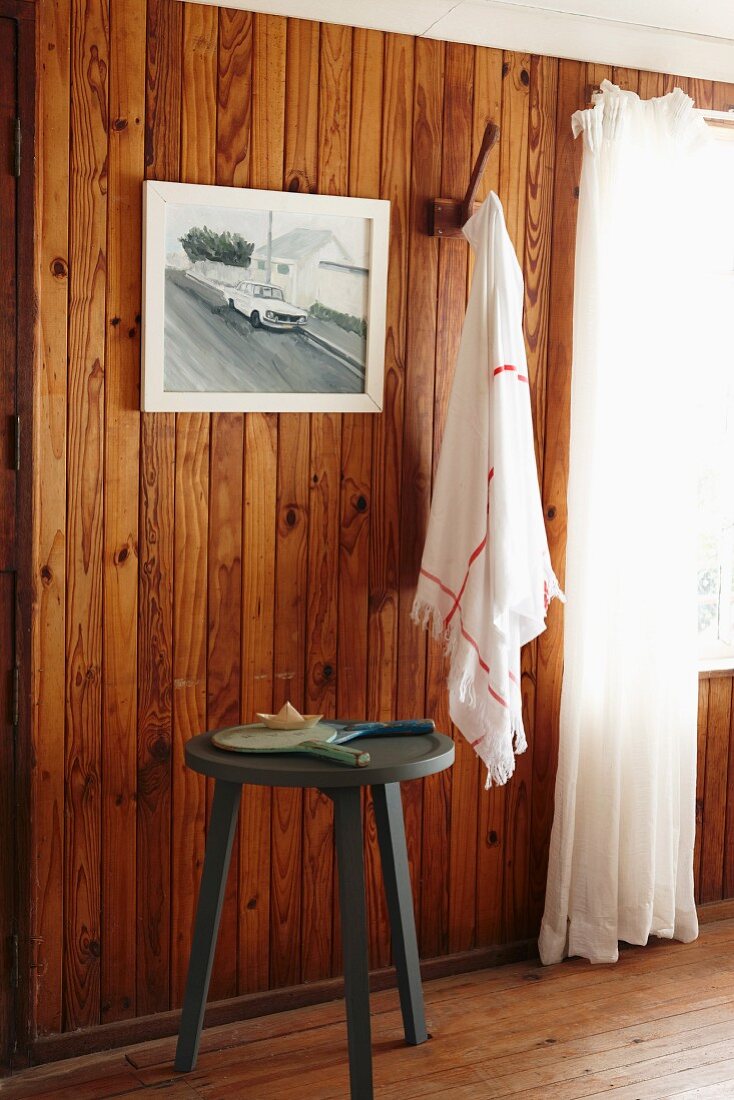 Three legged stool in front of a wood paneled wall with a photograph and towel hanging from a hook