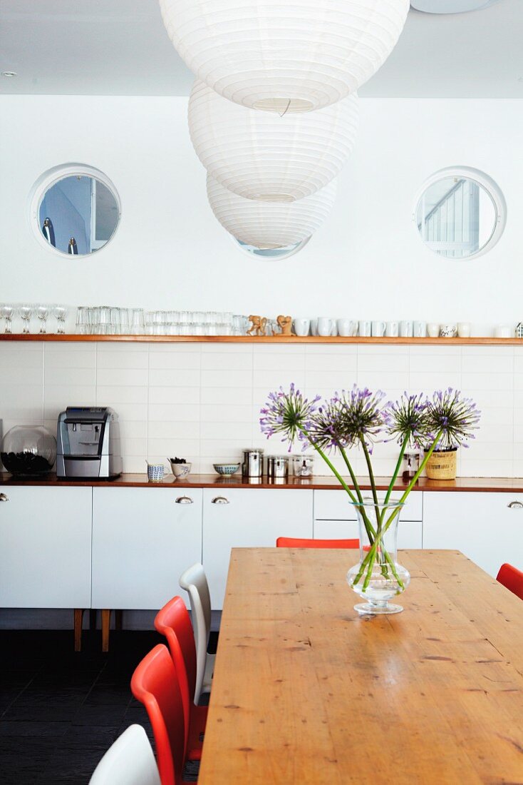 Drei Bullaugen über Küchenzeile mit einfachem Gläserbord und Hängelampen mit Papierschirm über Esstisch