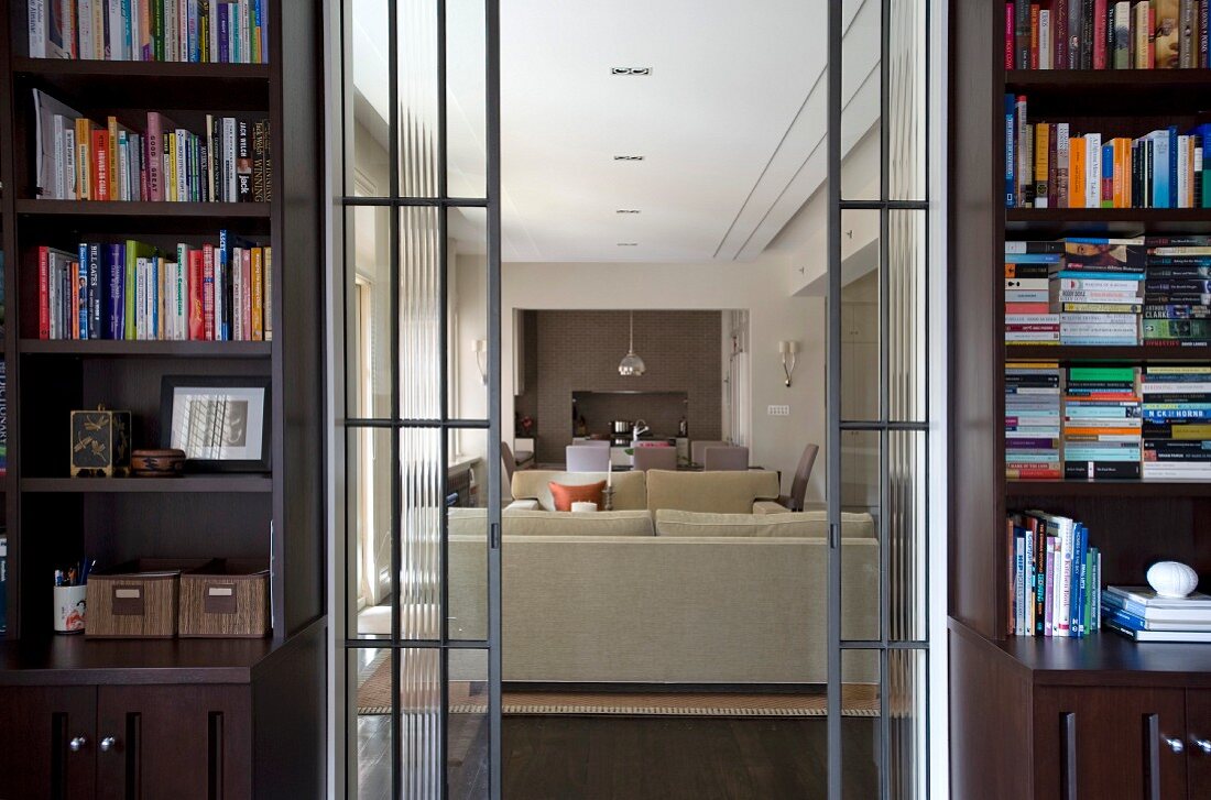 Open sliding glass doors flanked by bookcases and view of pale sofa set in modern living room