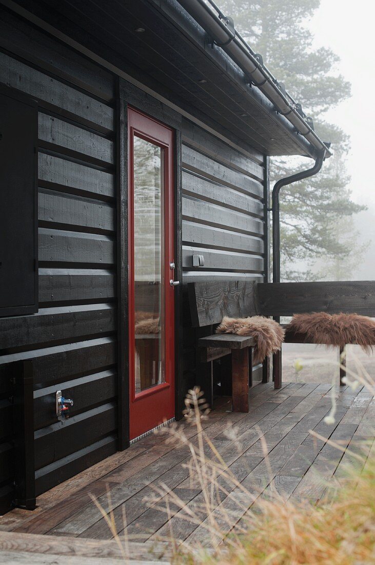Autumn mist over wooden house with terrace and wooden corner bench